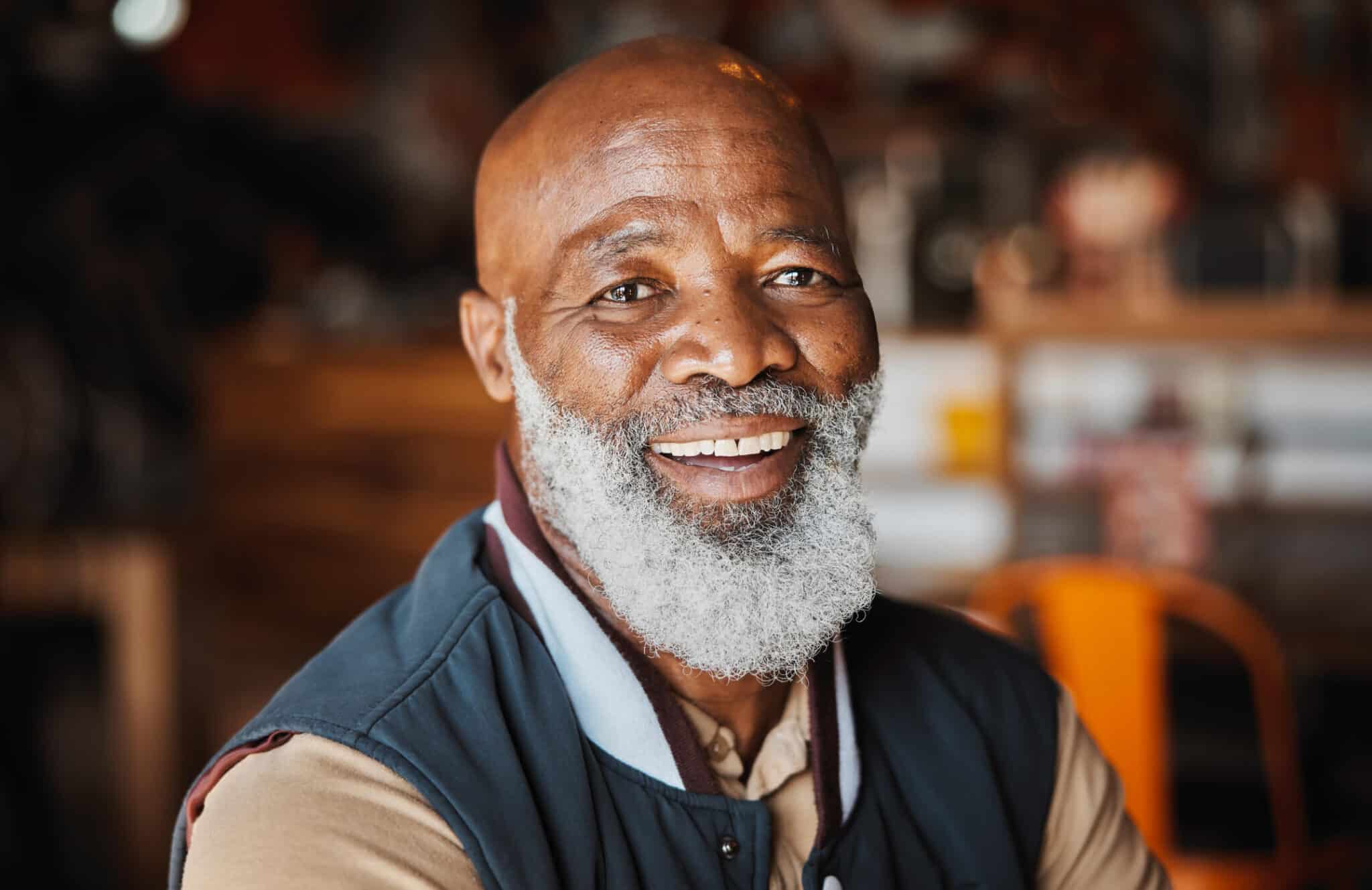 Older man sitting indoors, smiling at the camera